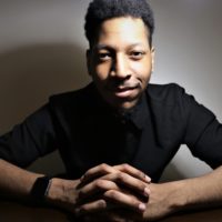A man posing with hands folded in a black shirt