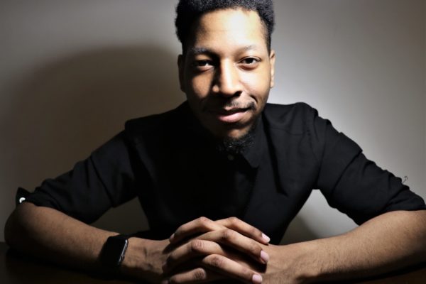 A man posing with hands folded in a black shirt