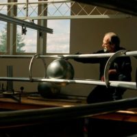 A caucasian man with grey hair with his kinetic, silver sculpture