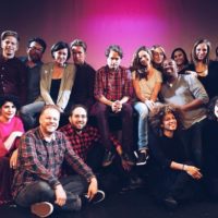 A group photo of the Experiments in Opera team against a dark pink background