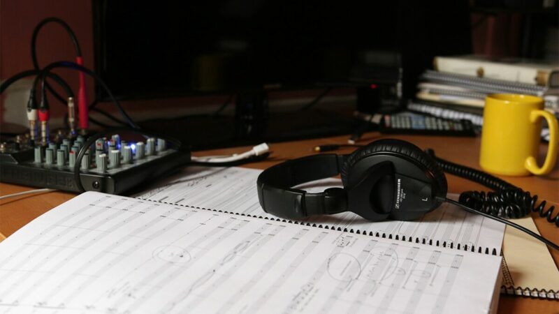 A printed score manuscript, headphones, and a coffee mug.