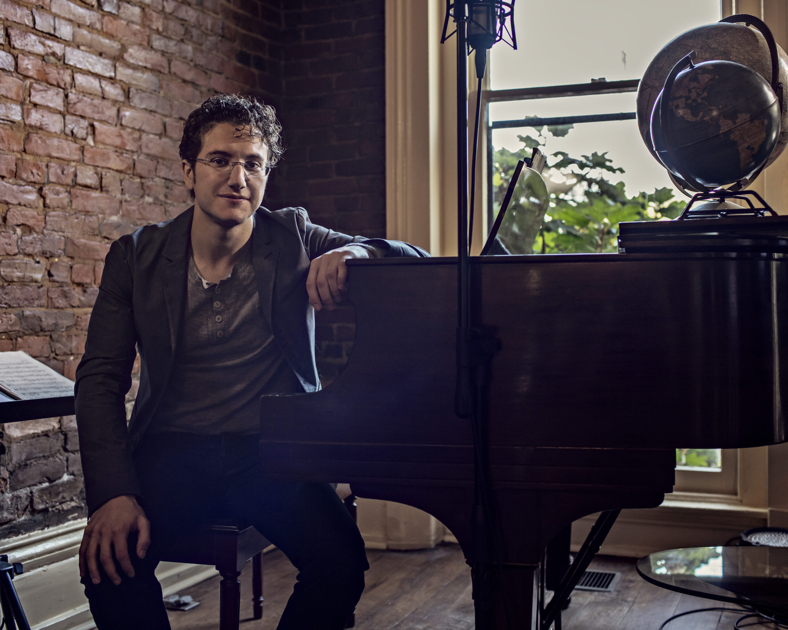 Teddy Abrams sitting at a grand piano which has a globe on top of it.